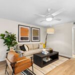 Winter Park, FL Apartments - The Taylor - Living Room with Ceiling Fan, Wooden Coffee Table, Neutral Couch, and Wood-Style Flooring