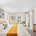 Two-Bedroom Apartments in Winter Park, FL - The Taylor - Bedroom with Entrance to Patio, Yellow Bedding, and Plush Carpeting
